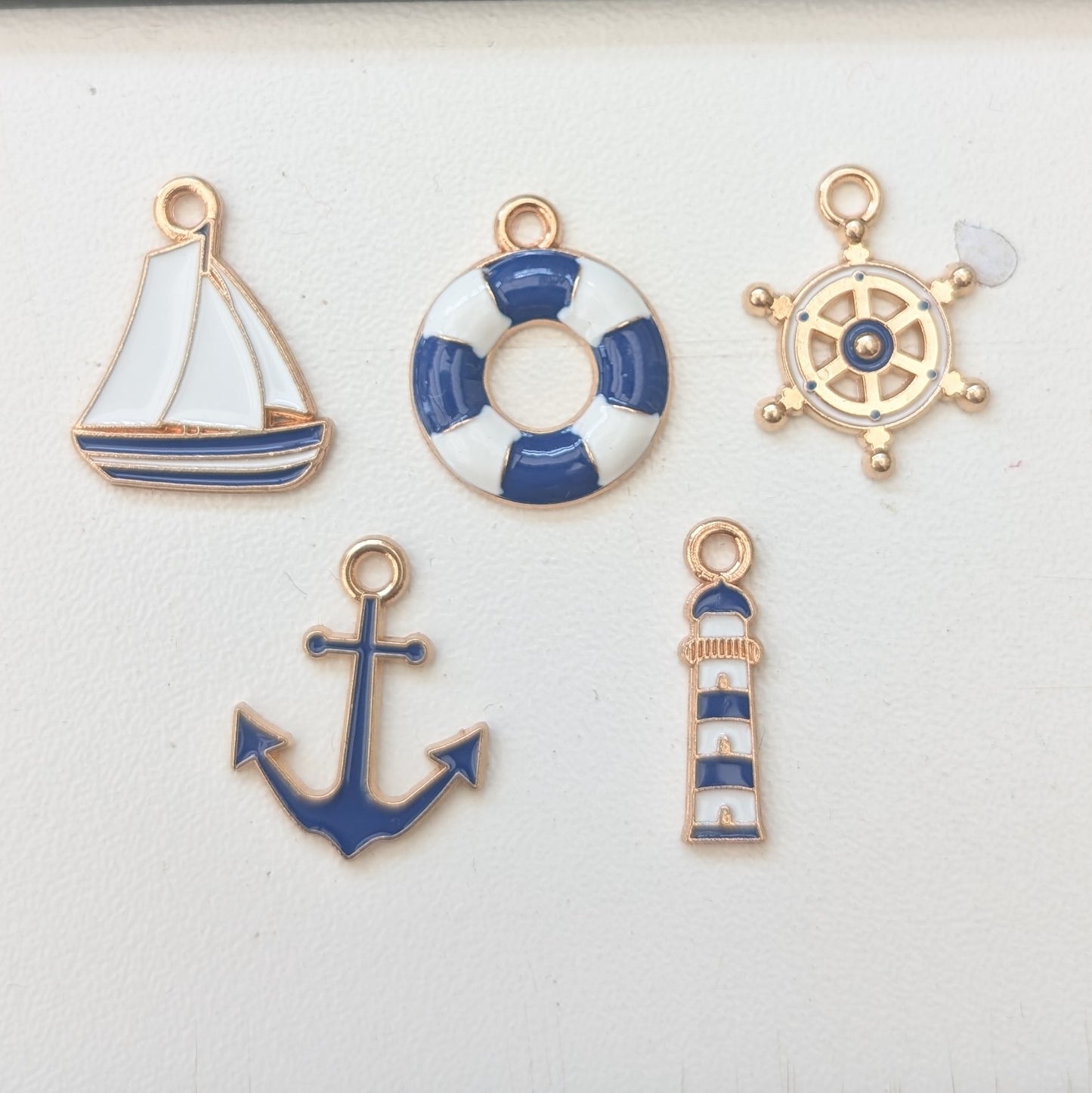 Set of nautical-themed charms including a sailboat, life buoy, wheel, anchor, and lighthouse on a white background.